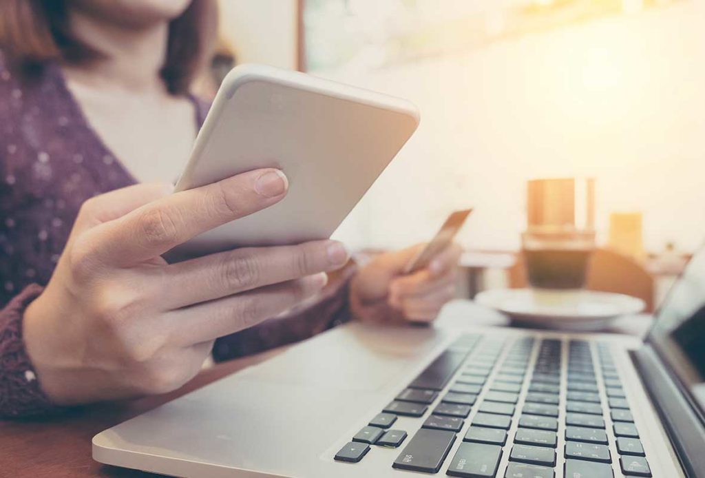 A woman holding a phone and a credit card sitting in front of an open laptop
