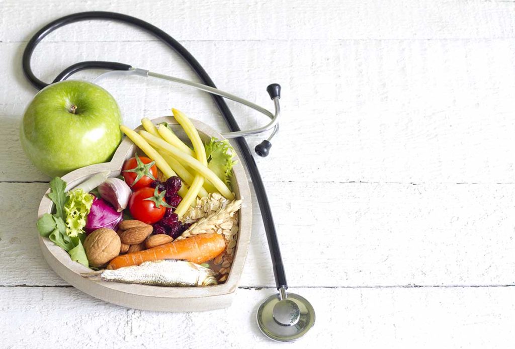 A stethoscope wrapped around a heart shaped bowl containing healthy foods