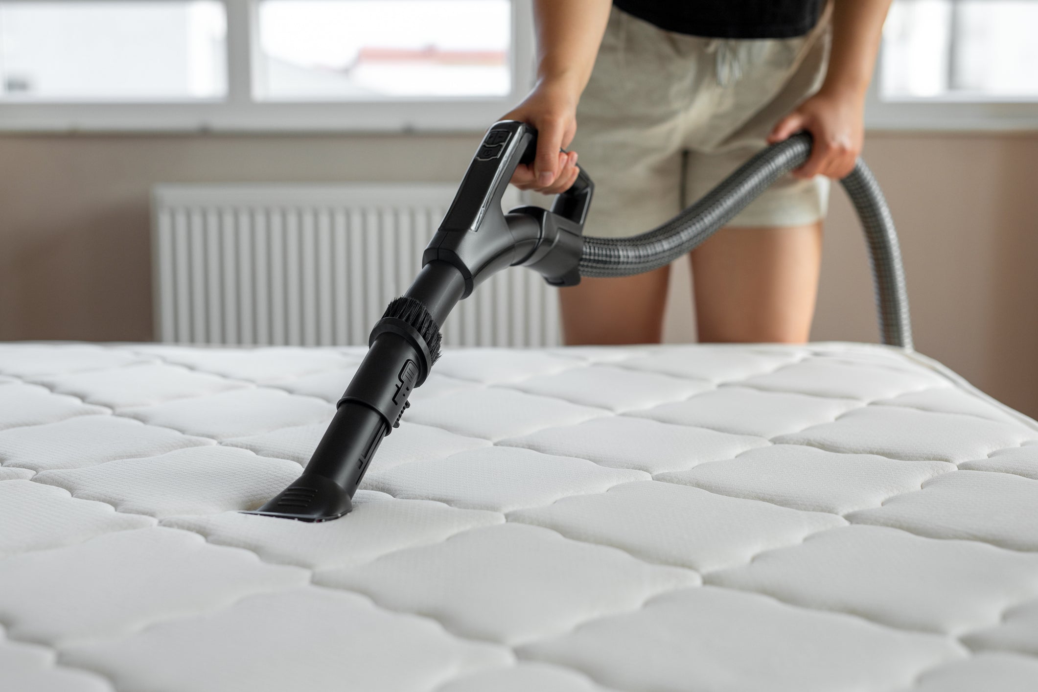 A woman cleaning the top of a mattress with a vacuum