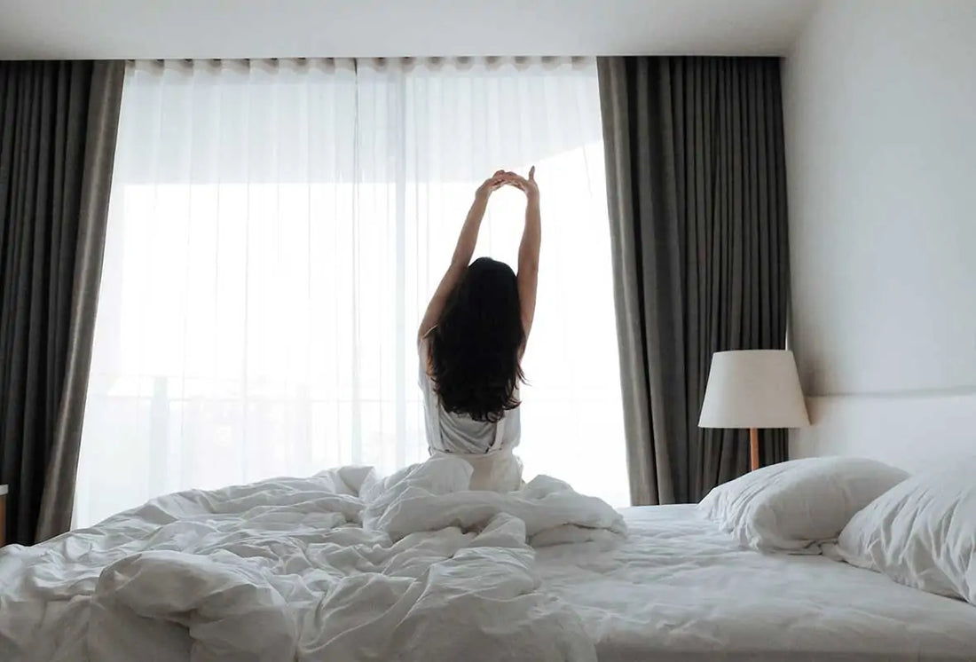 A woman sitting on her bed stretching in front of a window