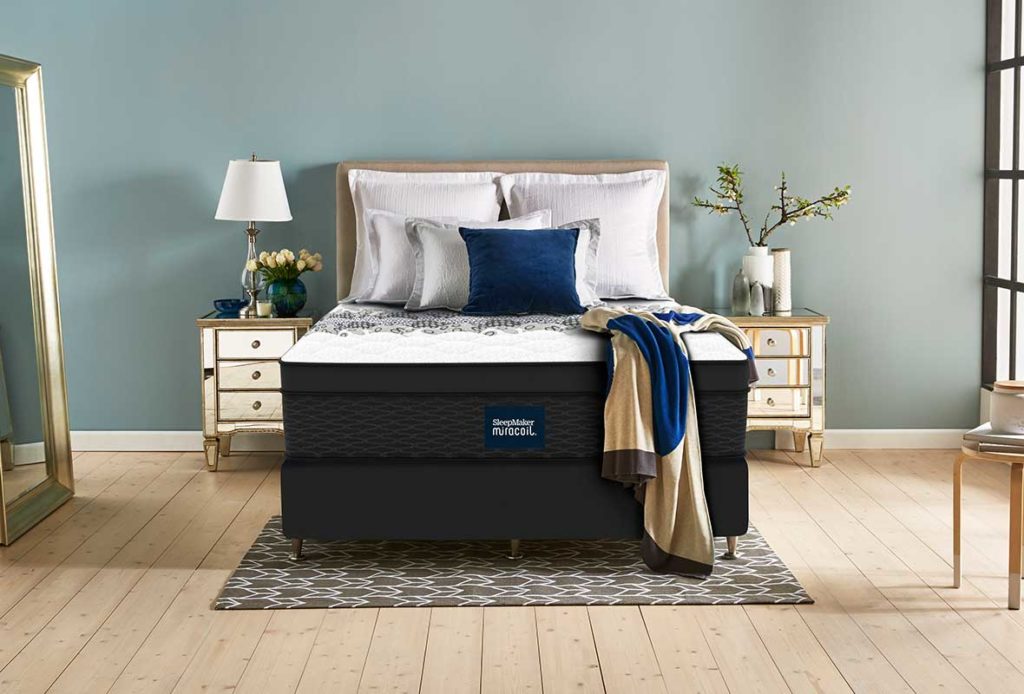 A SleepMaker Miracoil mattress dressed with pillows and blankets in a bedroom