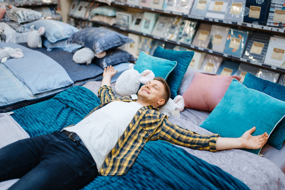 A man smiling and lying on a bed in a furniture store