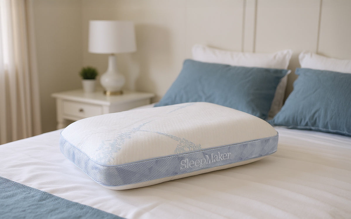 SleepMaker Advanced Sleep pillow on a bed with blue and white pillows in a bedroom setting.