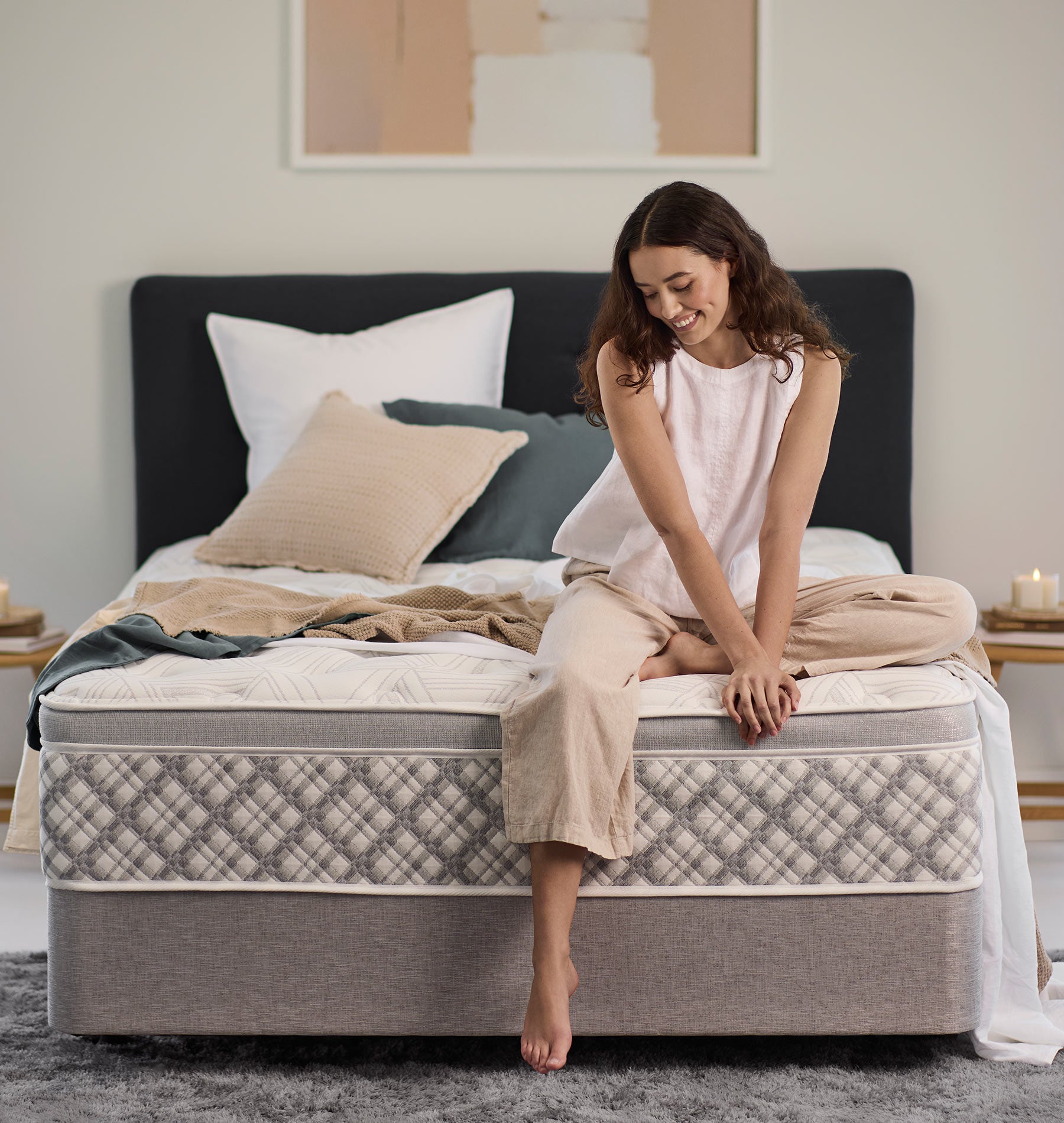 Woman sitting on a SleepMaker Performance mattress with blankets and pillows in a bedroom setting