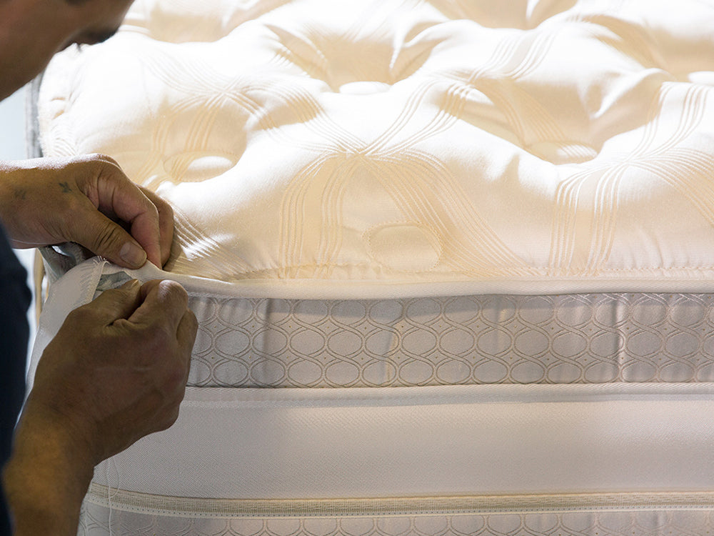 Person hand-stitching a mattress with a close-up view of the mattress cover