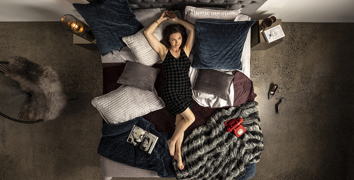 woman in black dress lying on a huge bed filled with pillows