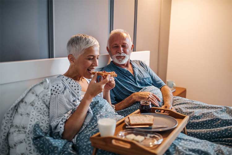 women eating bread on bed with husband looking at her 